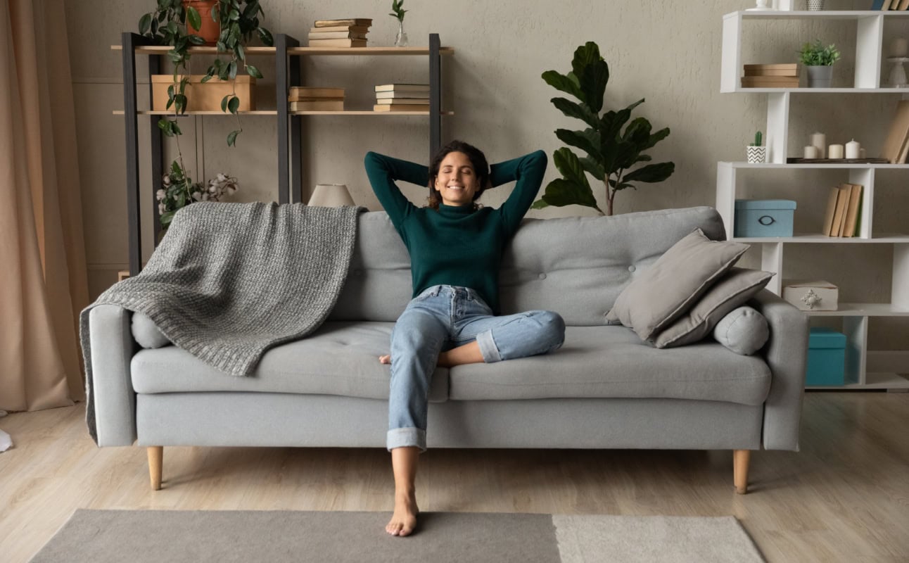 Woman sitting comfortably on a couch smiling with her hands behind her head.